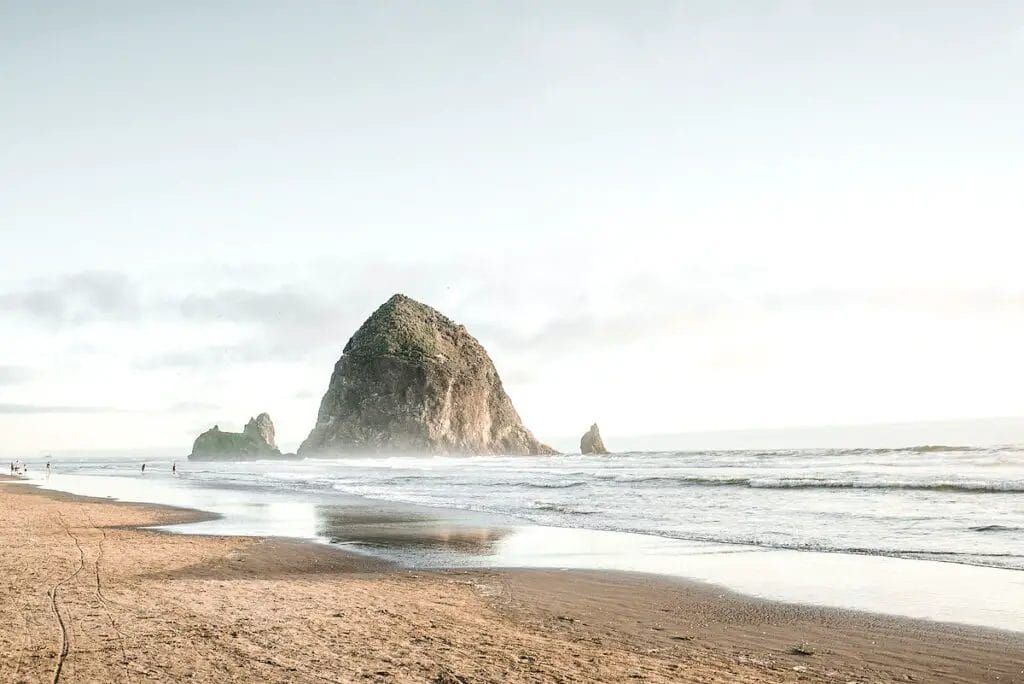 a beach with a large rock in the distance with Haystack Rock in the background