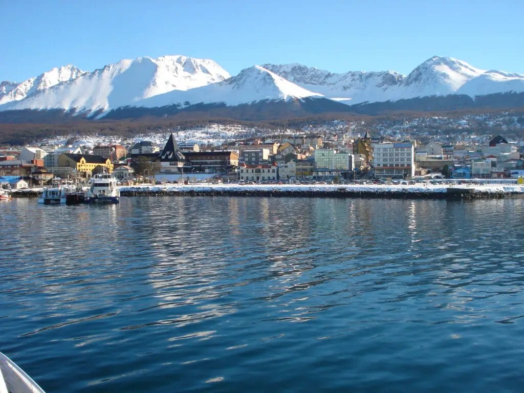 A City Next To Water With Snow Covered Mountains In The Background
