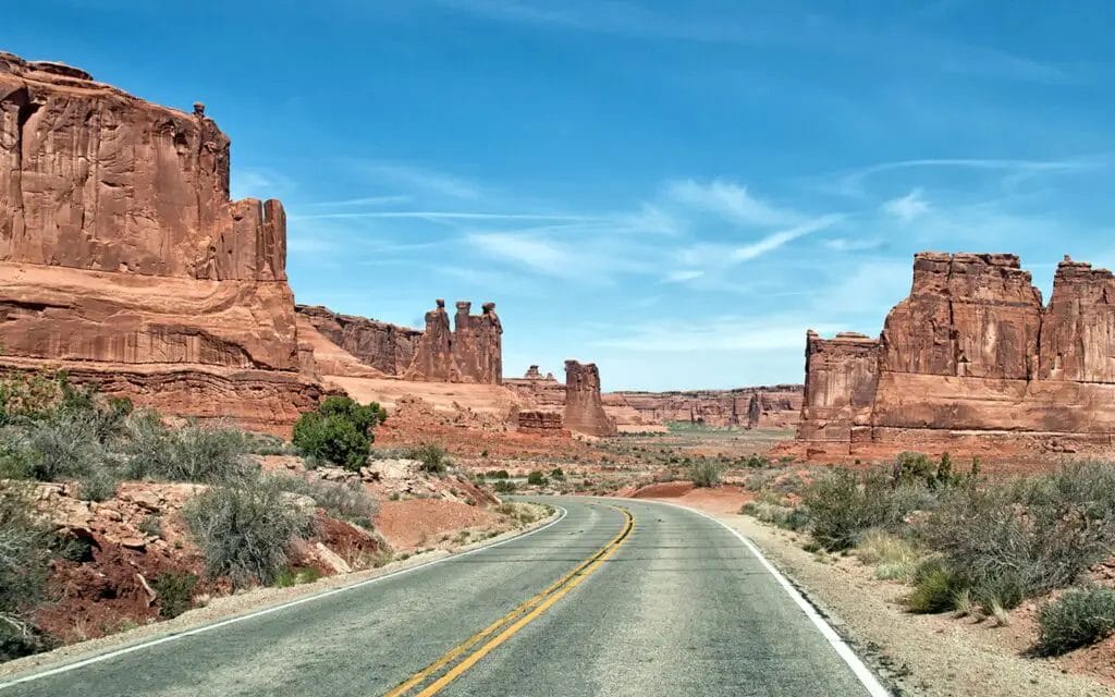 a road with red rock formations with Arches National Park in the background