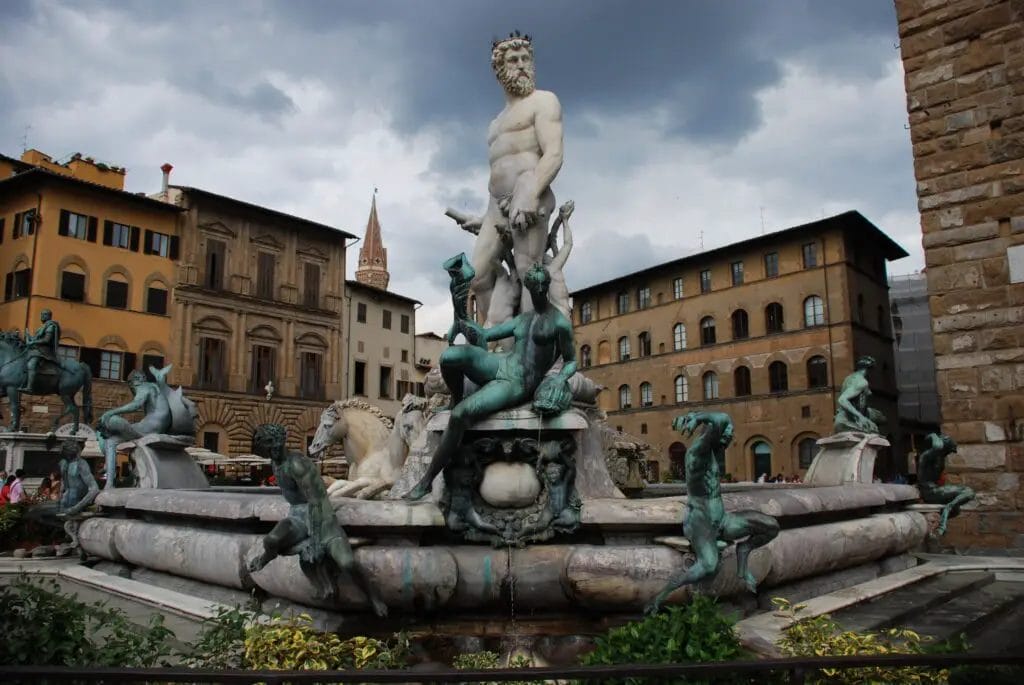 a statue of a person and a fountain in front of buildings with Fountain of Neptune, Florence in the background