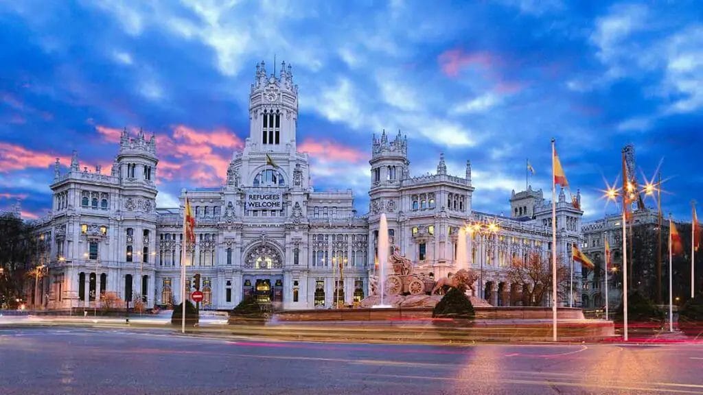 a large white building with a fountain in front with Plaza de Cibeles in the background